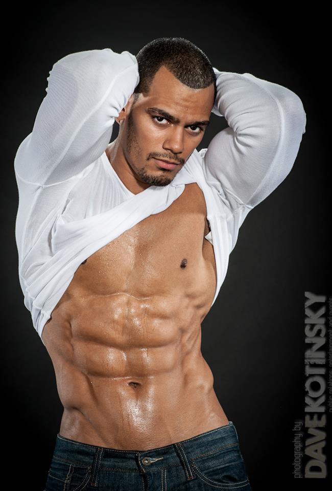 185011_10151112111698211_1244681905_n Man lifting shirt, displaying muscular, toned torso with six-pack abs, wearing jeans, against dark background.