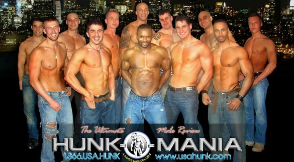 Group of shirtless men in jeans posing in front of a city skyline at night.
